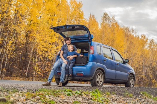 Dad and son are resting on the side of the road on a road trip. Road trip with children concept.