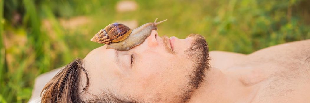 Young man makes a face mask with snail mucus. Snail crawling on a face mask. SPA for man, SPA for all. BANNER, LONG FORMAT