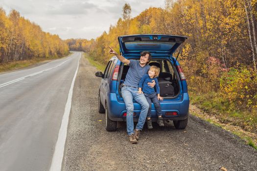 Dad and son are resting on the side of the road on a road trip. Road trip with children concept.