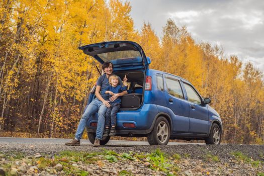 Dad and son are resting on the side of the road on a road trip. Road trip with children concept.