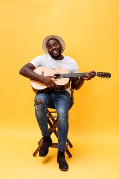 Full-length photo of excited artistic man playing his guitar. Isolated on yellow background