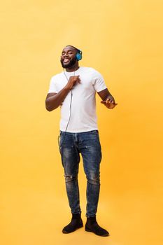 Full length portrait of a cherry young african american man listening to music with headphones and dancing isolated over yellow background.