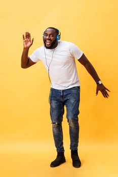 Full length portrait of a cherry young african american man listening to music with headphones and dancing isolated over yellow background.