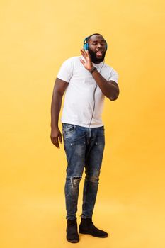 Full length portrait of a cherry young african american man listening to music with headphones and dancing isolated over yellow background.