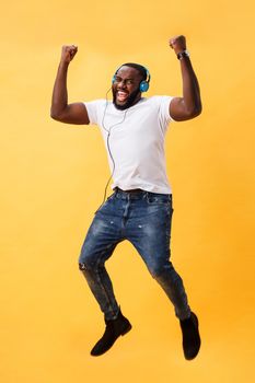 Full length portrait of a cherry young african american man listening to music with headphones and dancing isolated over yellow background.