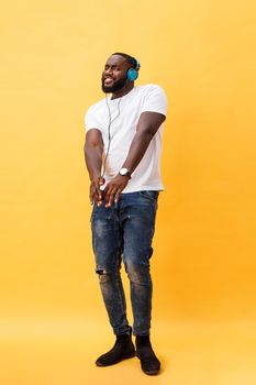 Full length portrait of a cherry young african american man listening to music with headphones and dancing isolated over yellow background.