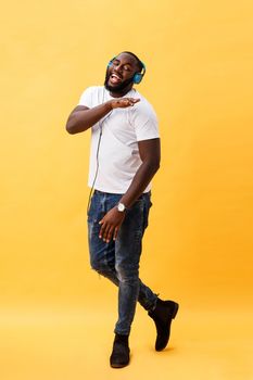 Full length portrait of a cherry young african american man listening to music with headphones and dancing isolated over yellow background.