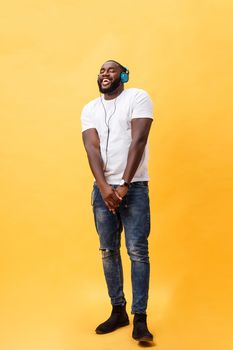 Full length portrait of a cherry young african american man listening to music with headphones and dancing isolated over yellow background.