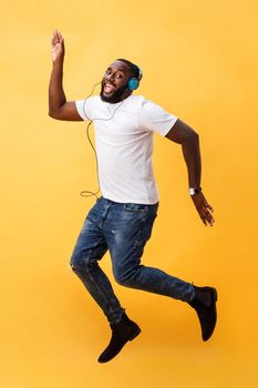 Full length portrait of a cherry young african american man listening to music with headphones and dancing isolated over yellow background.