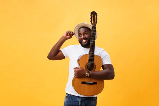 Muscular black man playing guitar, wearing jeans and white tank-top. Isolate over yellow background