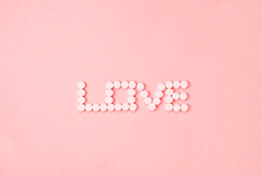Single word LOVE made with white pills on pink background, 