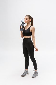 Side view full length portrait of a young healthy sports woman holding a water bottle isolated on a white background.