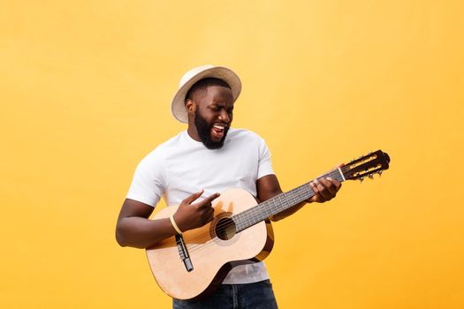 Muscular black man playing guitar, wearing jeans and white tank-top. Isolate over yellow background