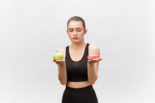 Young woman choosing between donut and apple on white background. Diet food concept.