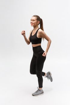 Full length picture of a sports woman running in studio over gray background