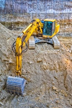 Yellow excavator with shovel in action at construction site. Vertical view