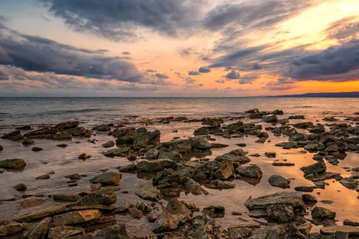 Stone beach at sunset. Twilight sea and sky. Dramatic sky and clouds. Nature landscape.