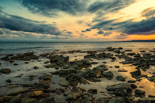 Stone beach at sunset. Twilight sea and sky. Dramatic sky and clouds. Nature landscape.