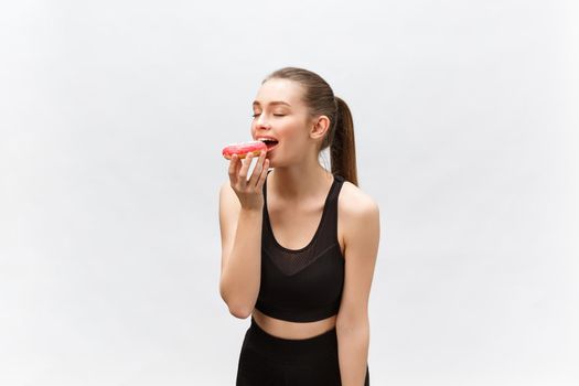Beautiful Fitness model wearing a black fitness outfit holding a junk food donut. Isolated over grey background