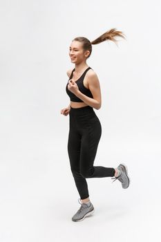 Full length picture of a sports woman running in studio over gray background