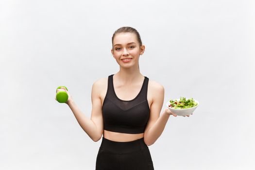 Sport, healthy lifestyle, people concept - young brunette woman with salad and a dumbbell. She is smiling and enjoying the healthy lifestyle