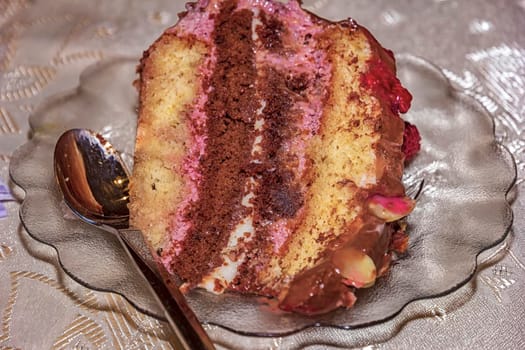 Close view of a delicate piece of chocolate cake, torte with nuts and fruits on a plate with a spoon. 