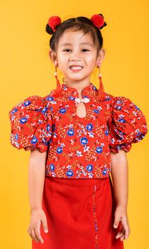 Happy Asian Chinese little girl smile wearing red cheongsam, Portrait children in traditional dress with greeting gesture celebration for Chinese New Year, studio short isolated on yellow background