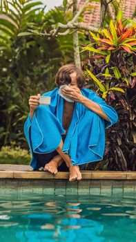 Sick man traveler. The man caught a cold on vacation, sits sad at the pool drinking tea and blows his nose into a napkin. His son is healthy and swimming in the pool. Travel insurance concept. VERTICAL FORMAT for Instagram mobile story or stories size. Mobile wallpaper