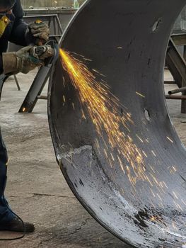 Fly bright sparks from the angle grinder machine. A young male welder in gloves grinds a metal product with angle grinder