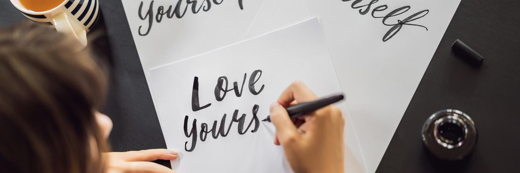 BANNER, LONG FORMAT Love yourself. Calligrapher Young Woman writes phrase on white paper. Inscribing ornamental decorated letters. Calligraphy, graphic design, lettering, handwriting, creation concept.