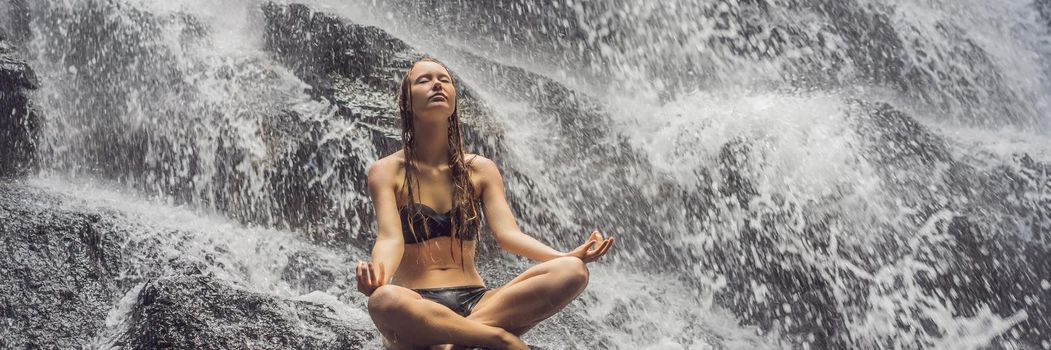 Wellness spa, vacation and yoga meditation concept. Young woman sitting in lotus position on the rock in tropical waterfall. BANNER, LONG FORMAT