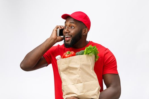 Delivery Concept - Portrait of Handsome African American delivery man or courier with grocery package and talking on mobile phone to check the order. Isolated on Grey studio Background.