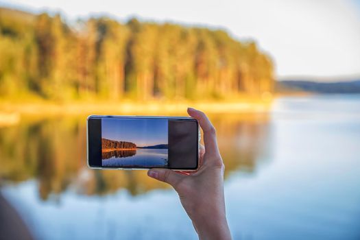 Woman hand holding smartphone taking photo picture of beautiful nature / mobile phone photography and video concept