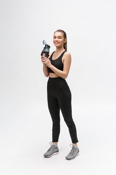 Side view full length portrait of a young healthy sports woman holding a water bottle isolated on a white background.