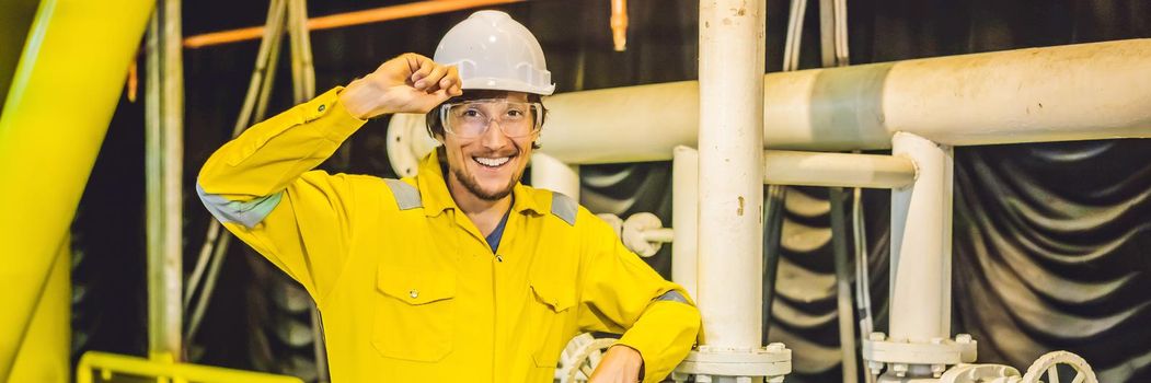 Young man in a yellow work uniform, glasses and helmet in industrial environment,oil Platform or liquefied gas plant. BANNER, LONG FORMAT