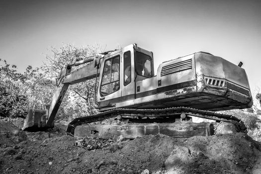 Crawler excavator during earthmoving works on construction site in black and white