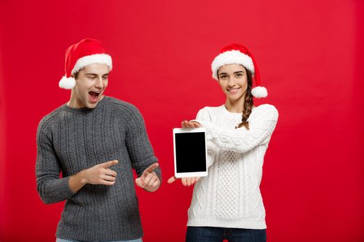 Christmas concept - Happy young couple in christmas sweaters surprising something in digital tablet.