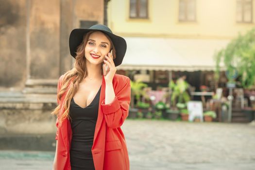 Long haired lady in fashionable black hat calling by mobile phone on the street of old city.