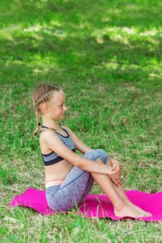 Little girl is sitting on a roll mat wearing sportswear in the public park.
