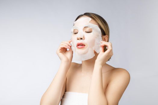 Beautiful asian woman applying paper sheet mask on her face white background.