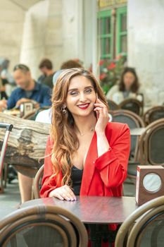 Fashionable woman is talking by mobile phone sitting outdoors at urban cafe.