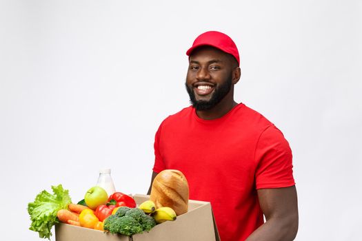 Delivery Concept - Handsome African American delivery man carrying package box of grocery food and drink from store. Isolated on Grey studio Background. Copy Space.