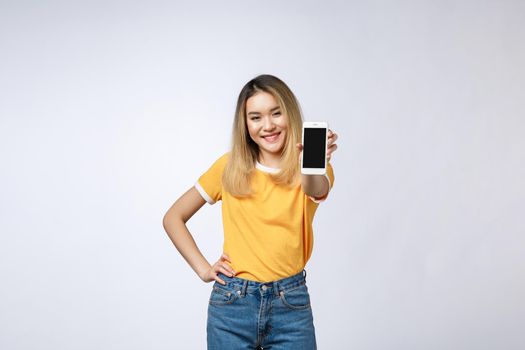 Close up portrait of a smiling asian woman showing blank screen mobile phone while standing isolated over gray background