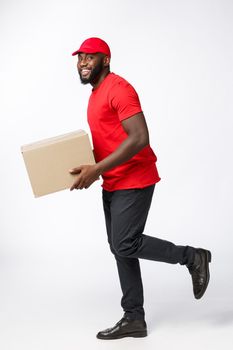 Portrait of Happy African American delivery man in red cloth walking to send a box package to customer. Isolated on Grey studio Background. Copy Space.