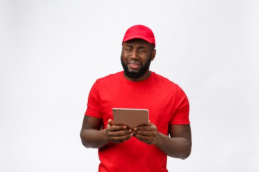 Delivery Concept - Portrait of Serious African American delivery man with tablet in silly aggressive expression and unhappy. Isolated on Grey studio Background. Copy Space
