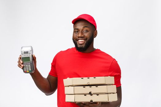 Happy young African American delivery man holding up an electronic card payment machine and delivery product. Isolated over grey background.