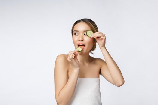 Young asian woman holding and eating cucumber slice in her hands isolated on white background.