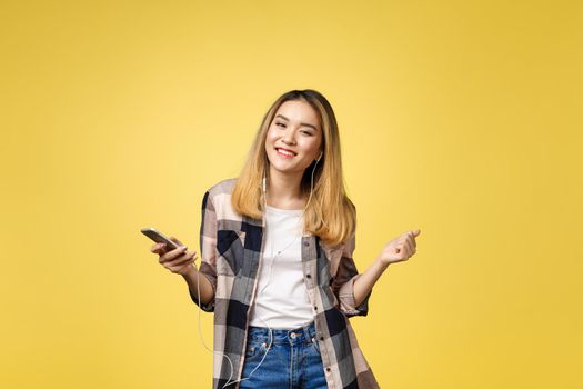 Fashion smiling asian woman listening to music in earphones over yellow background