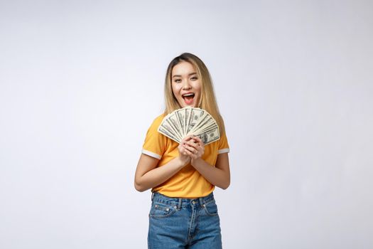 Asian woman holding cash notes isolated in white background. Young asian woman in white t-shirt in winning surprise, holding dollar note. Young rich hipster concept