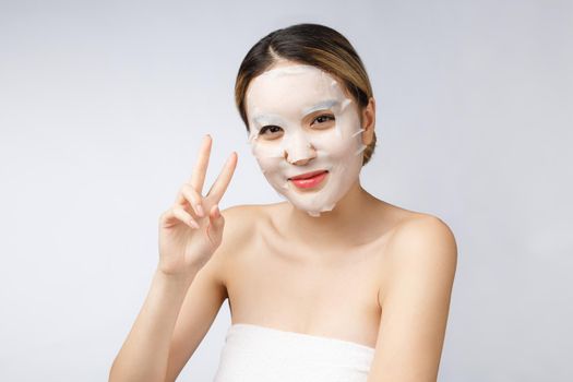 Beautiful asian woman applying paper sheet mask on her face white background